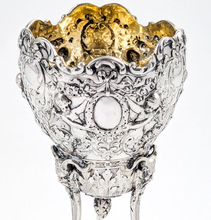 Hanau sterling silver tripod cup with repoussé putti, floral garlands, and ram’s head feet, Baroque Revival, c. 1880s